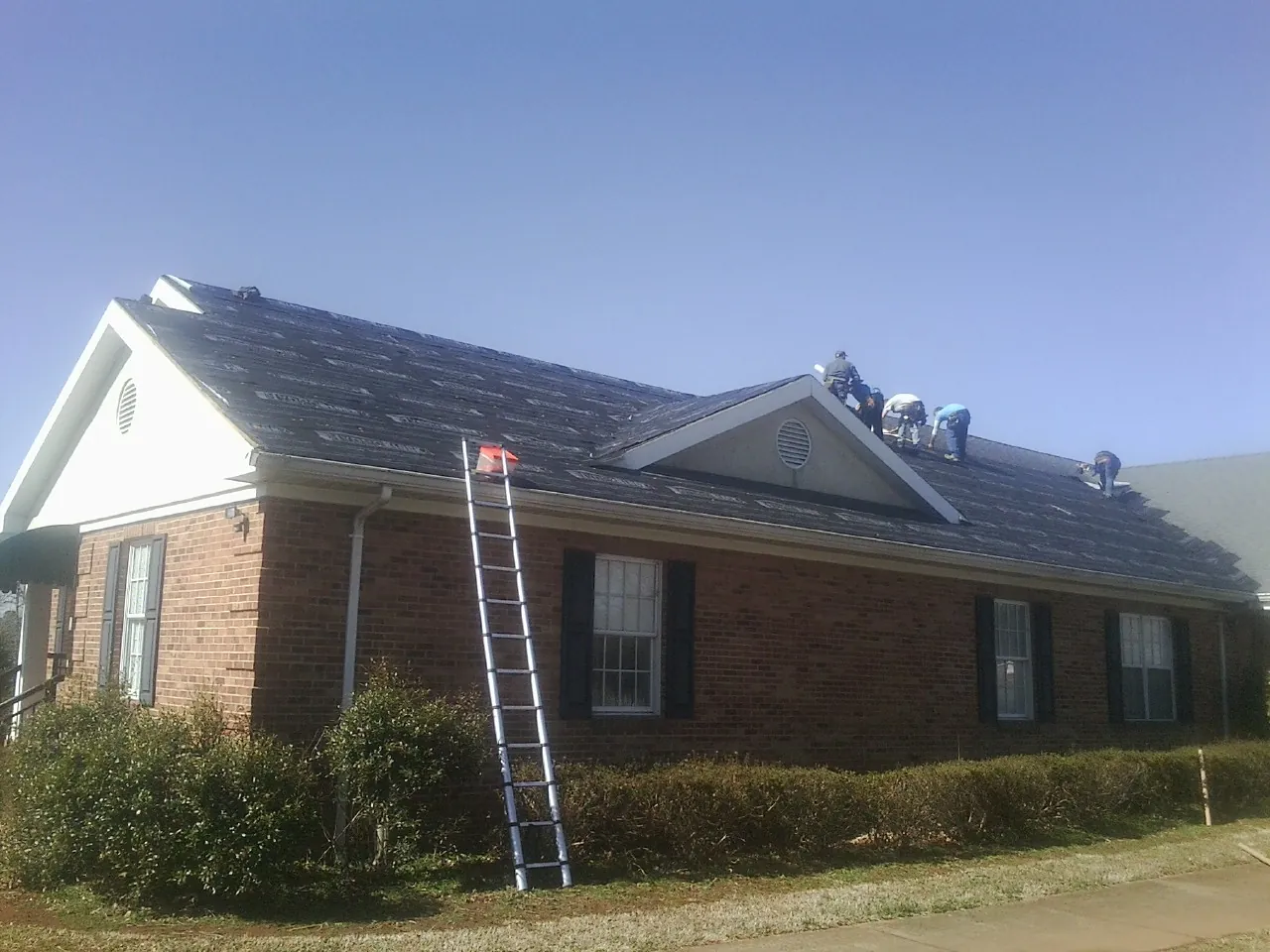 Crew tearing shingles off a brick ranch roof with a ladder set — Metal Roof Repair work by our crew in Indian Mound
