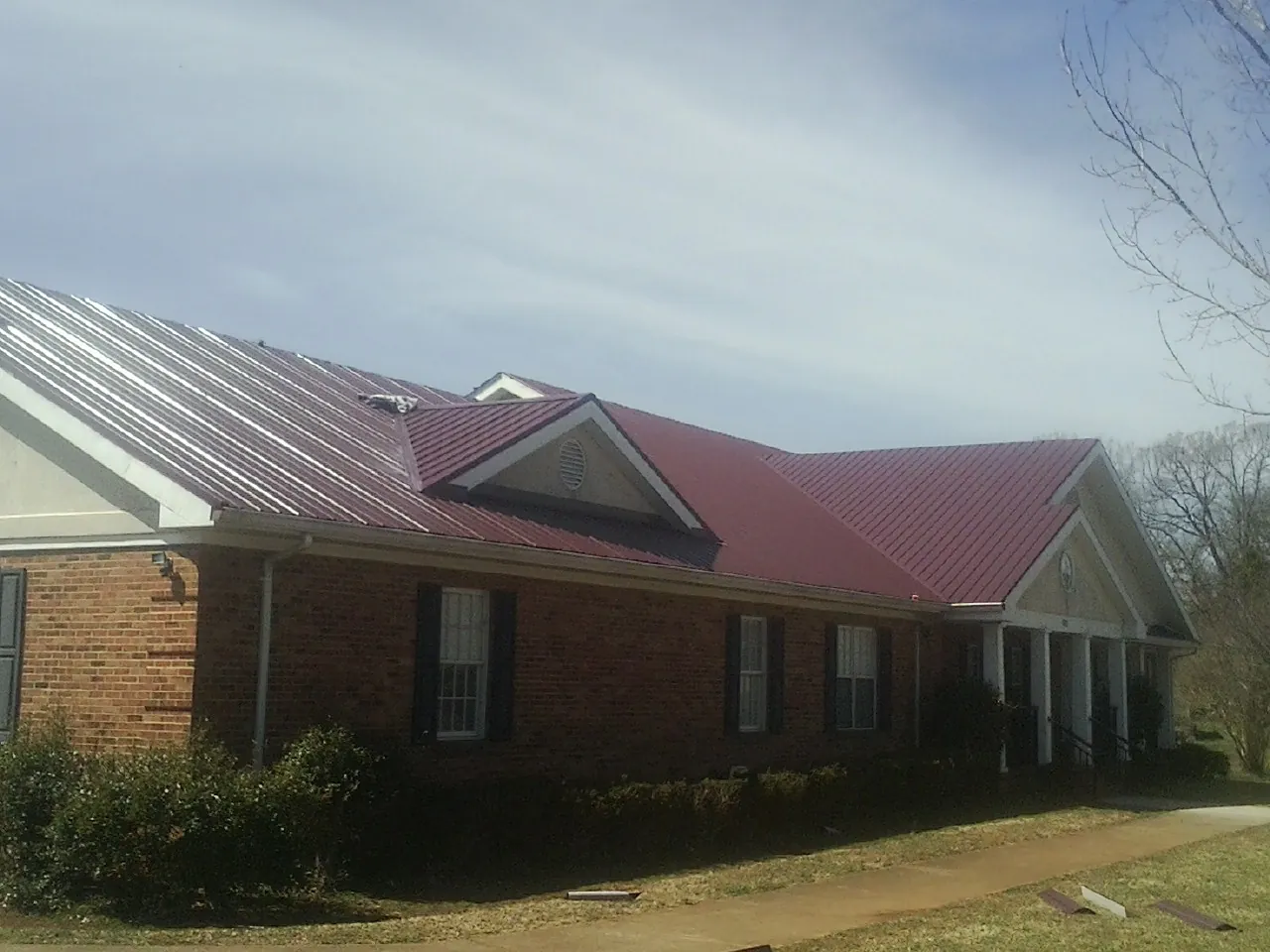 Red metal roof with gabled entries on a long brick building, from a Hail Damage Roof Repair job in Indian Mound
