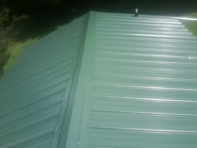New green metal panels meeting at the ridge of a roof — Flat Roof Repair work by our crew in Indian Mound