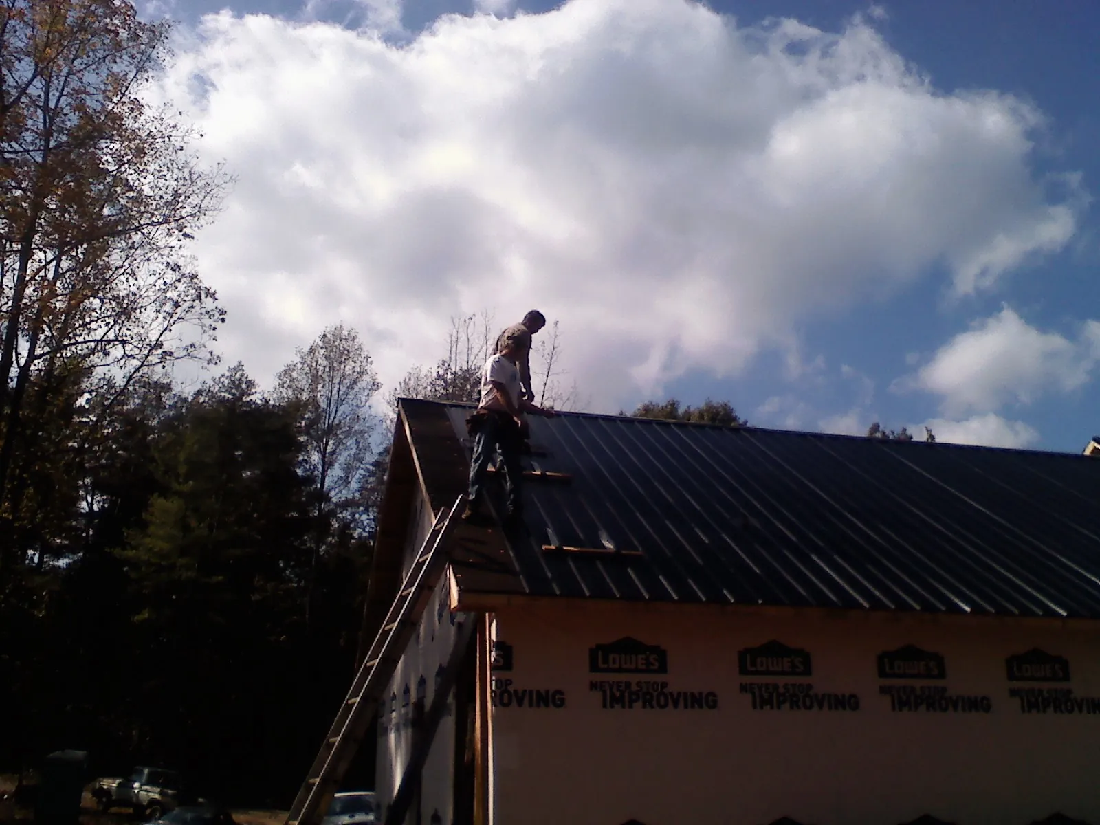Roofer fastening dark metal panels high against a cloudy sky, from a Roof Inspection job in Indian Mound
