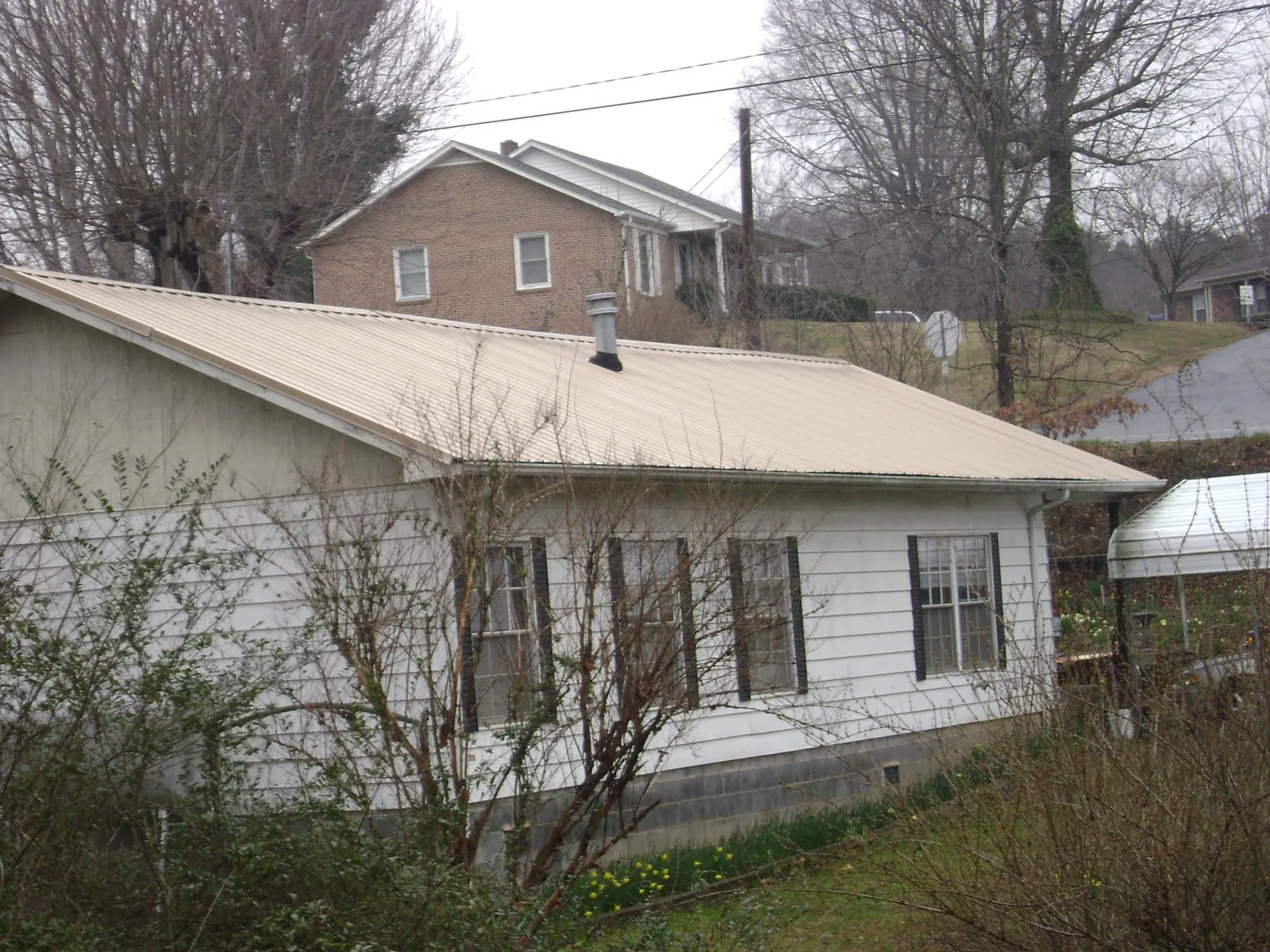 Tan metal roof on a white sided house set into a hillside — Commercial Roofing by Roofing Brothers in Indian Mound